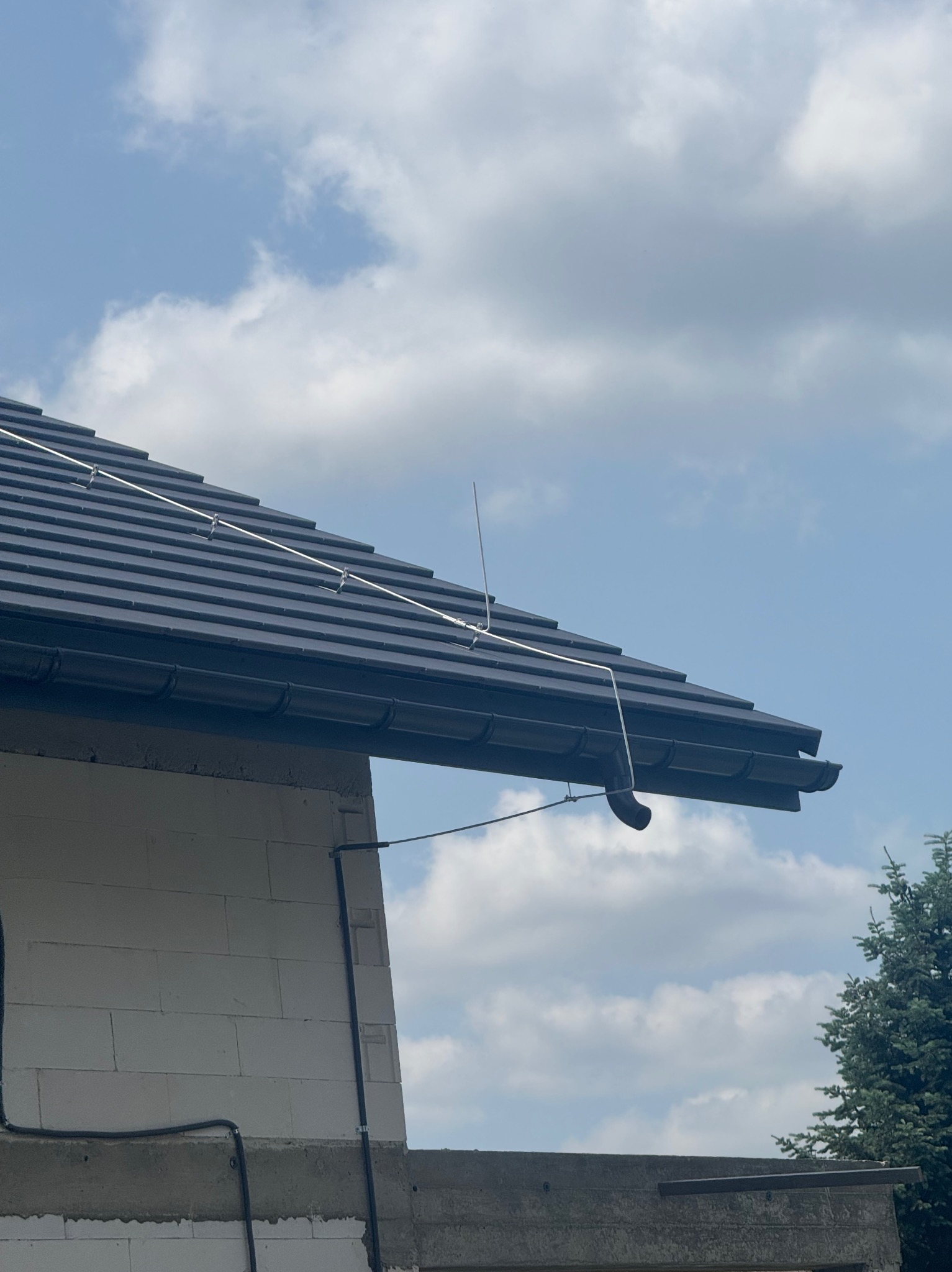 Zabezpieczenie domu w Świętoszówce: Instalacja odgromowa na dachu z czarnej dachówki, widoczne przewody i maszt. Ochrona przed wyładowaniami atmosferycznymi.