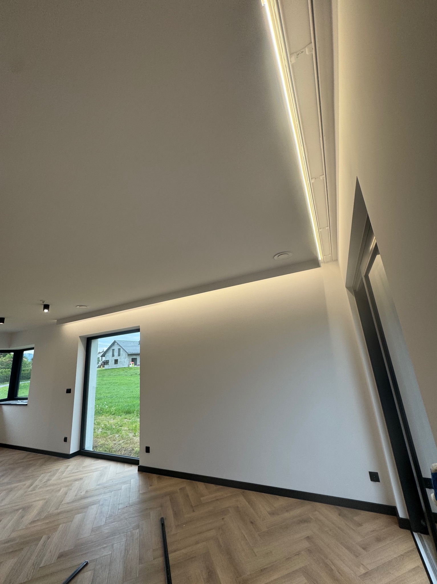 Nowoczesne wnętrze z parkietem w jodełkę i subtelnym oświetleniem LED w listwach sufitowych, podkreślającym minimalistyczny design pomieszczenia.