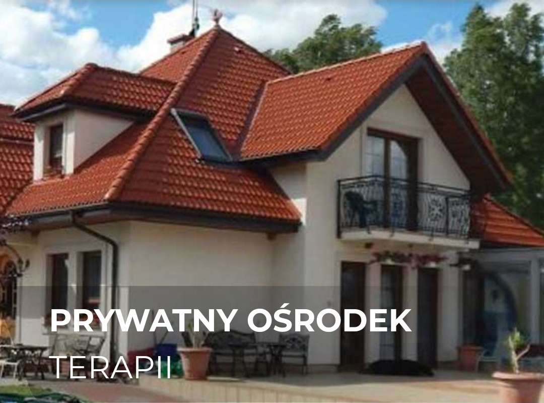 Dwupiętrowy budynek z czerwonym dachem i balkonem z kutą balustradą, otoczony zielenią, stylizowany na prywatny ośrodek.