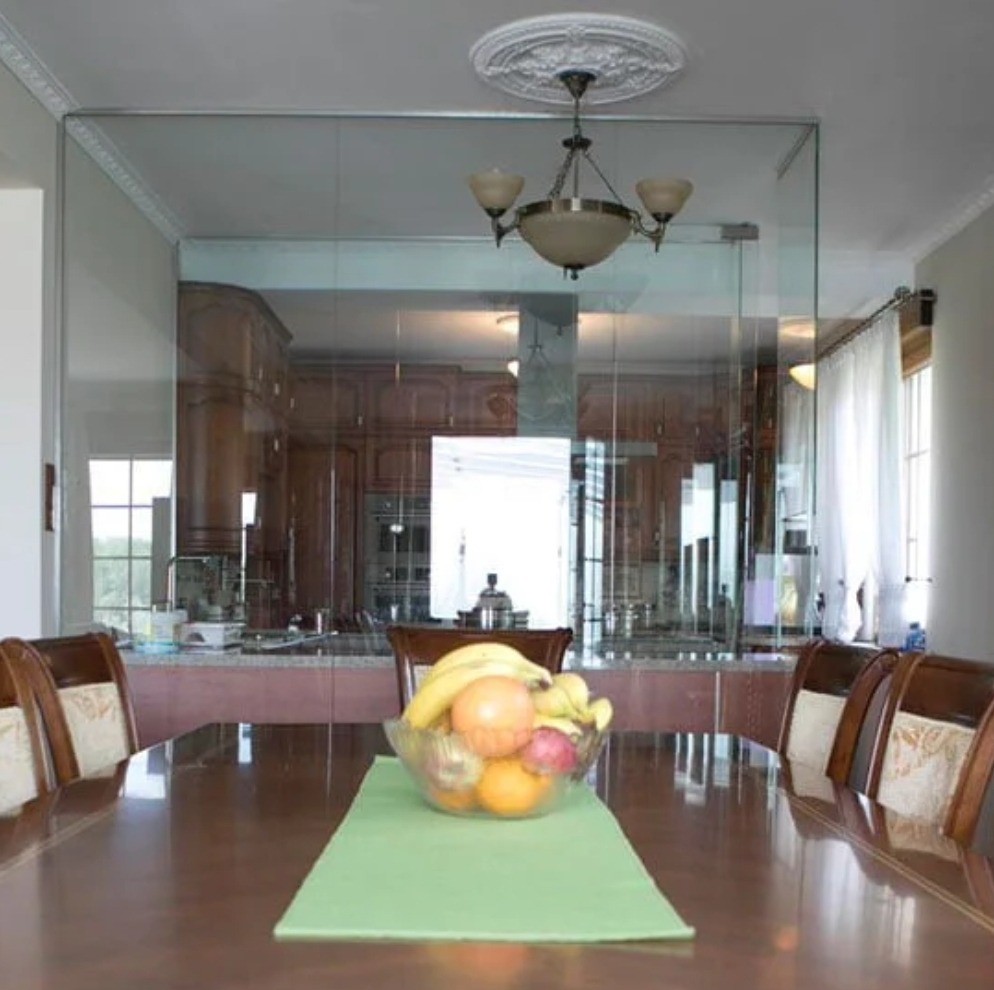 Jadalnia z szklaną ścianą oddzielającą kuchnię, stół z owocami w misie i zielonym bieżnikiem, widoczny żyrandol i dekoracyjny sufit.