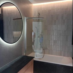 TOM-BUD - Nowoczesna łazienka z podświetlanym lustrem, kabiną prysznicową i wanną obłożoną czarnym marmurem, oświetlenie LED podszafkowe i sufitowe.