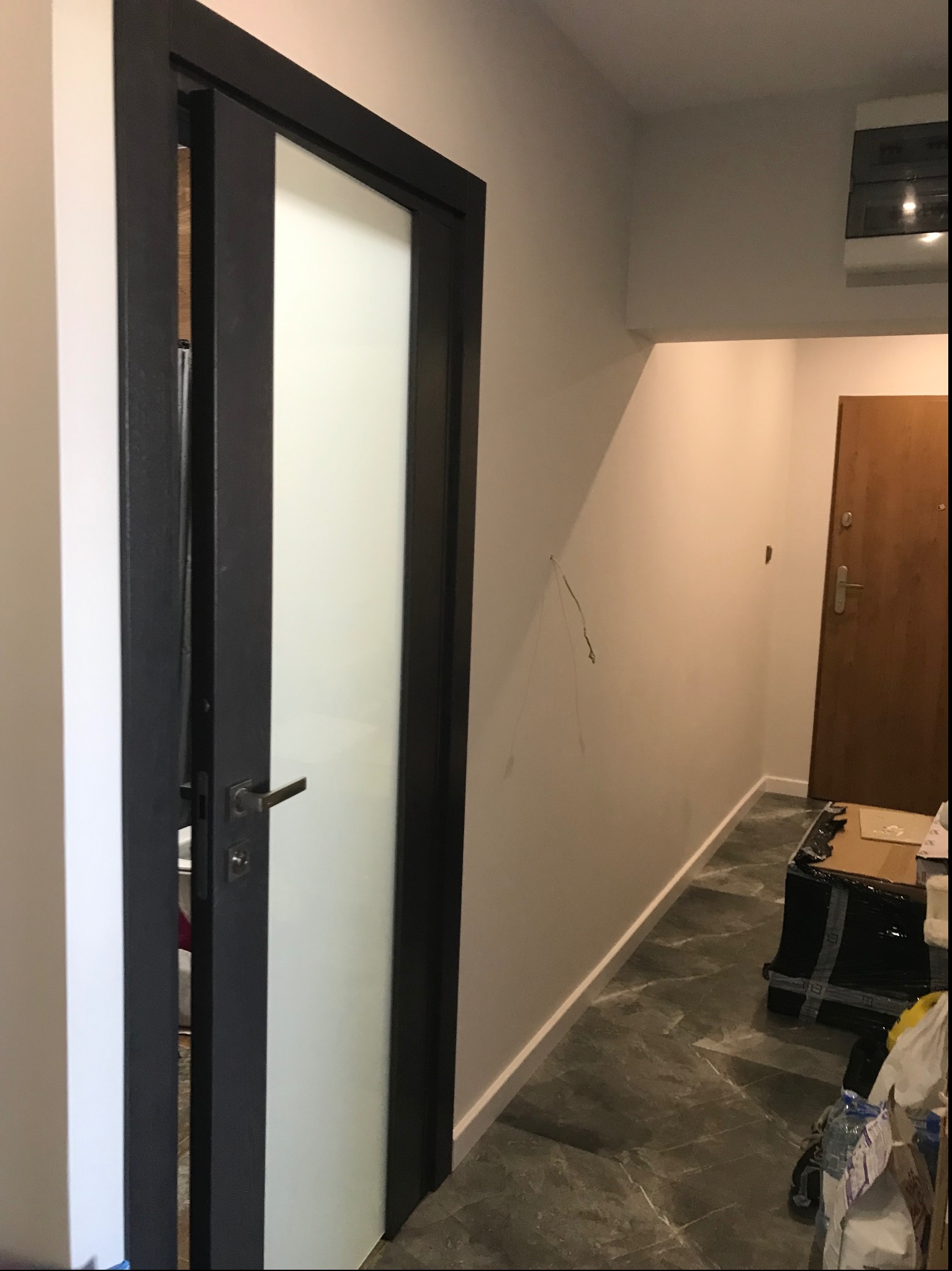 Częściowo przesuwne drzwi wewnętrzne z czarną ramą i matową szybą, widoczne w korytarzu z marmurową podłogą i sprzętem AGD na ścianie.