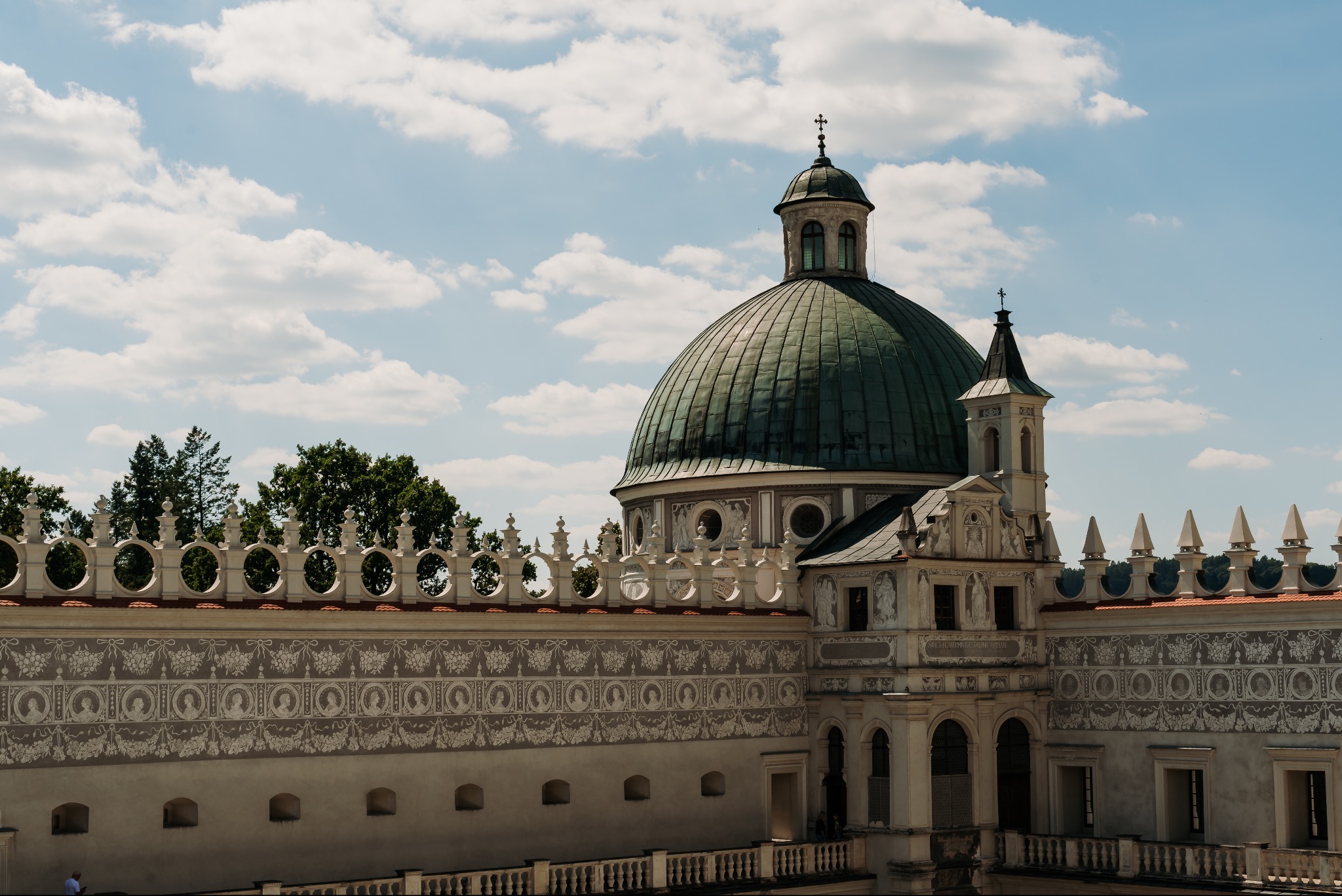Barokowa architektura: Zamek z zieloną kopułą i ozdobnymi fryzami pod błękitnym niebem z chmurami.
