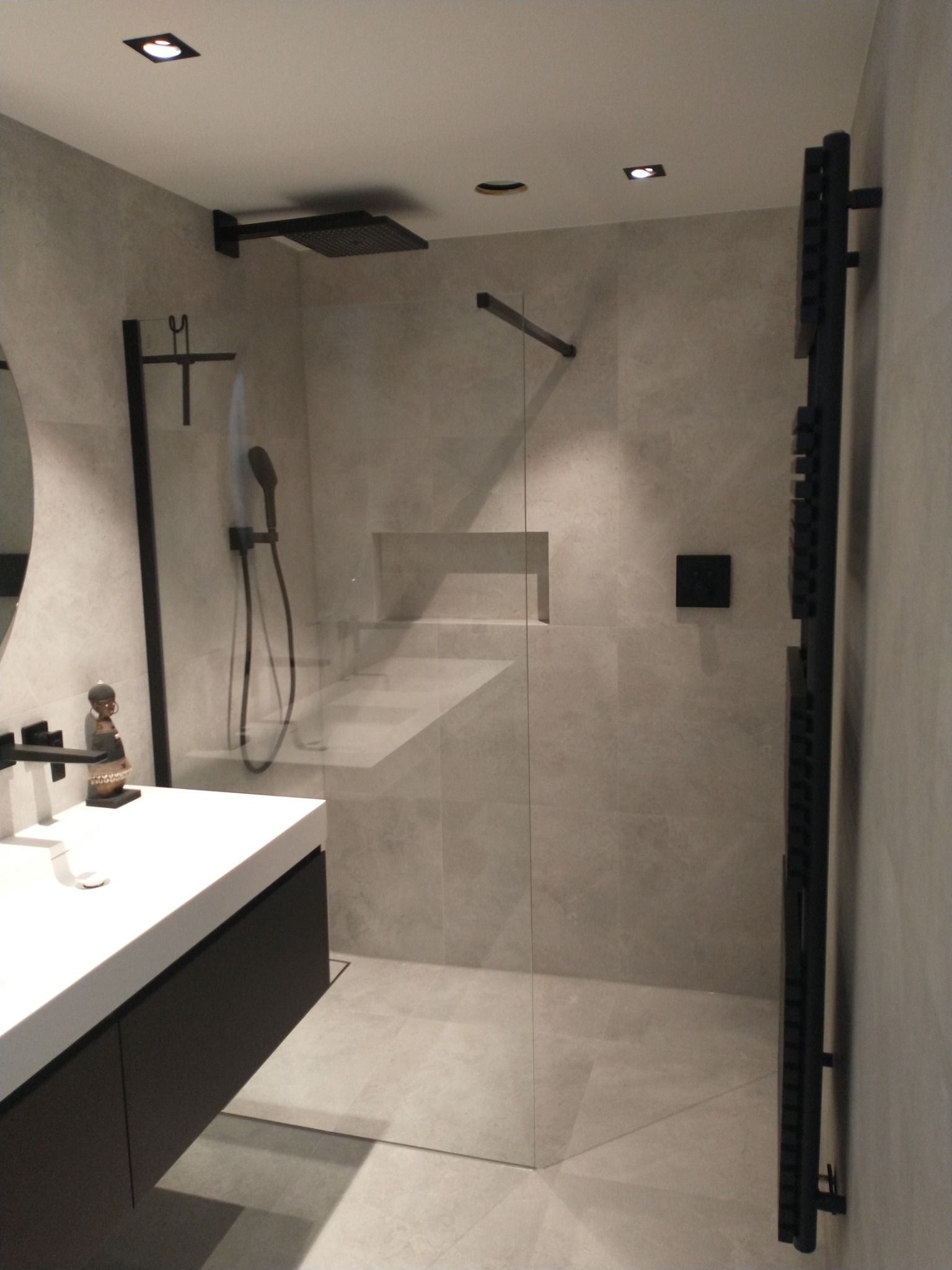 Nowoczesna łazienka z kabiną typu walk-in, czarna armatura, grzejnik drabinkowy i umywalka z szafką w kolorze antracytowym, dekoracyjna figurka na blacie.