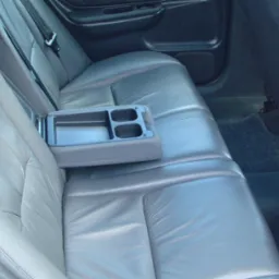 Wnętrze samochodu z szarą skórzaną tapicerką tylnej kanapy i rozkładanym podłokietnikiem z uchwytami na napoje.