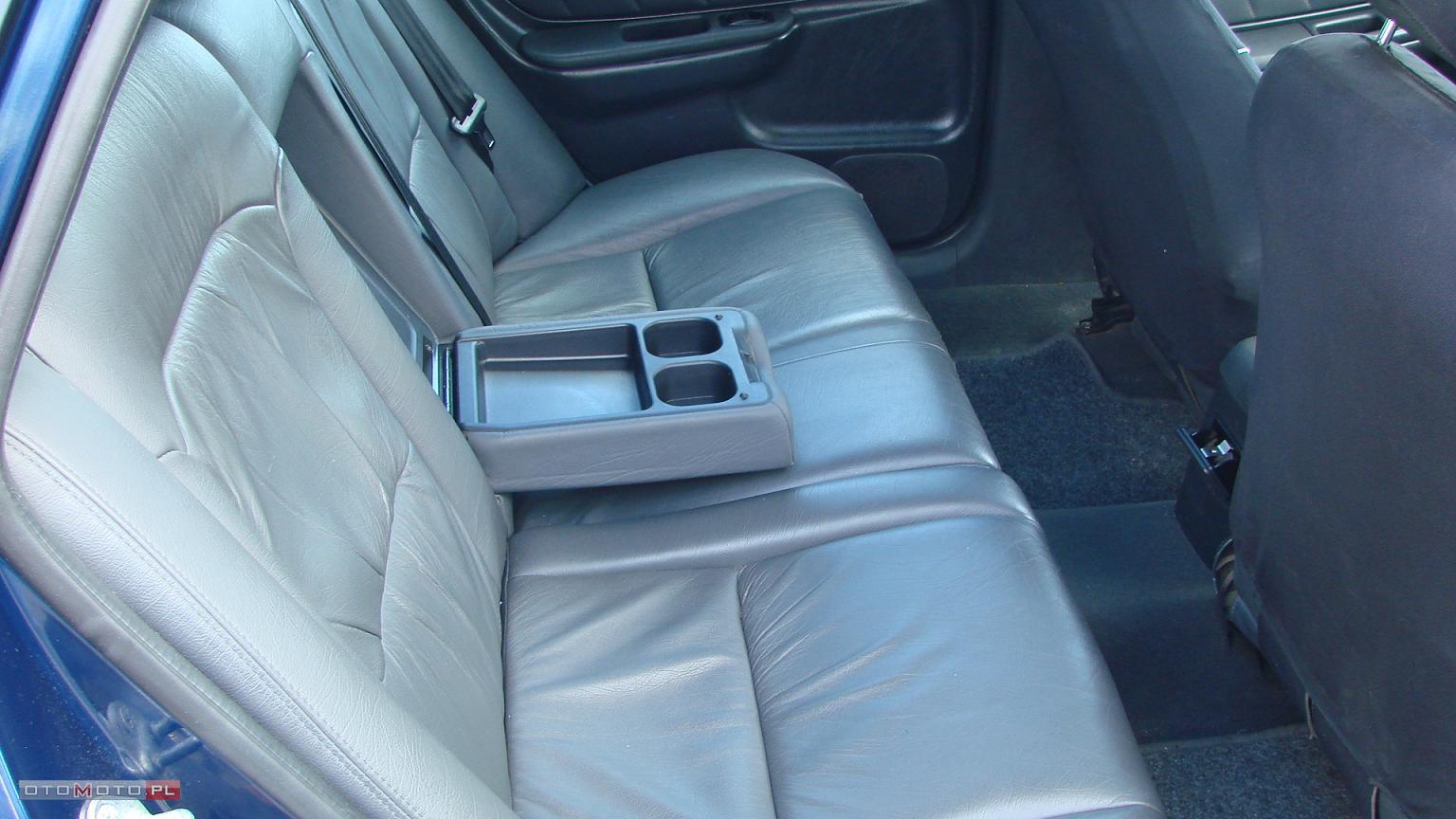 Wnętrze samochodu z szarą skórzaną tapicerką tylnej kanapy i rozkładanym podłokietnikiem z uchwytami na napoje.