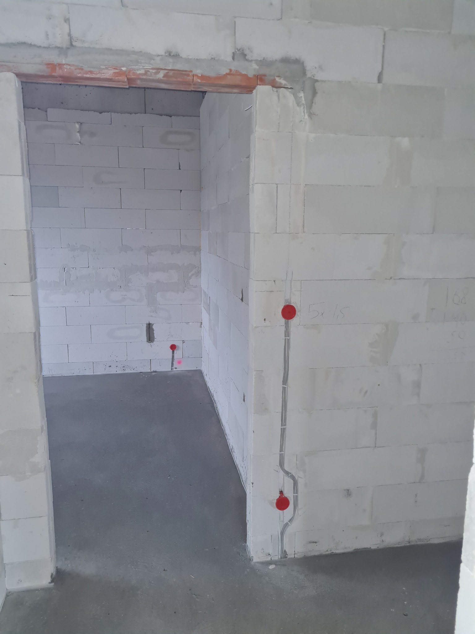 Wewnętrzne ściany z betonu komórkowego w trakcie budowy, widoczne poprowadzone kable elektryczne z czerwonymi puszkami pod gniazdka i włączniki.