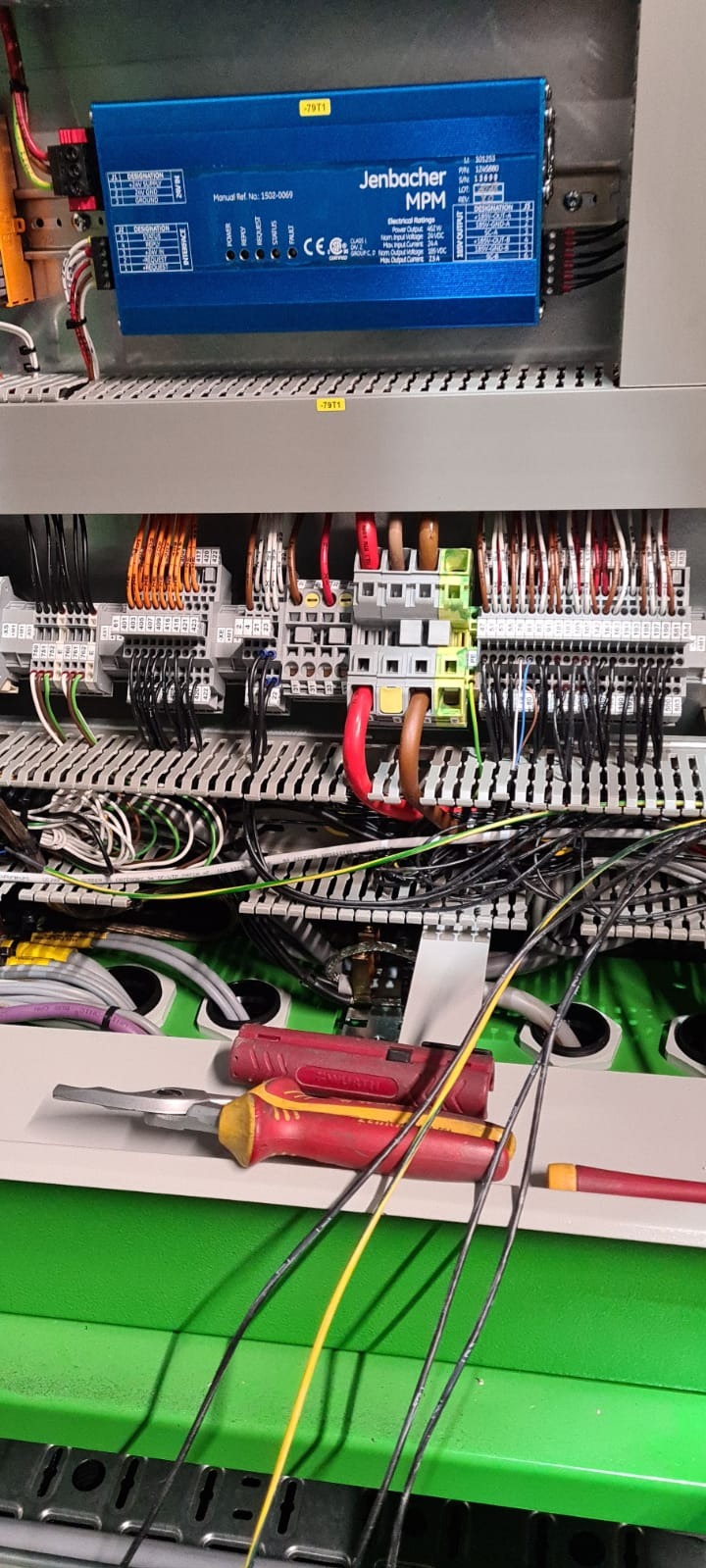 Rozdzielnica elektryczna w trakcie montażu, widoczne okablowanie, listwy zaciskowe, moduł Jenbacher MPM i narzędzia: dwa wkrętaki Wera z czerwono-żółtymi rękojeściami i szczypce do ściągania izolacji.