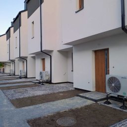 CMM KLIMAT MICHAŁ CYPRYŃSKI - Zewnętrzne jednostki klimatyzacji zamontowane na wspornikach przy szeregowych domach jednorodzinnych z białymi elewacjami i brązowymi drzwiami wejściowymi, widok z poziomu gruntu na nowo...