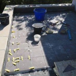 Łukasz - Montaż grafitowych płytek na tarasie, z widocznymi krzyżykami dystansowymi, wiadrami i narzędziami glazurniczymi.