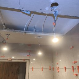 Łukasz - Układanie płytek w trakcie prac wykończeniowych w łazience w Łańcucie, widoczne krzyżyki dystansowe i podwieszany sufit z instalacją elektryczną.