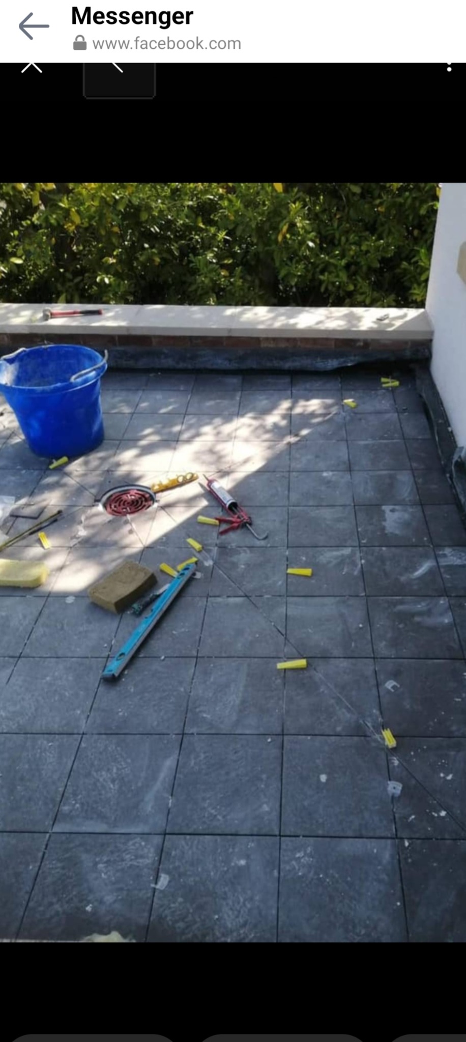 Układanie ciemnoszarych płytek na balkonie, widoczne narzędzia: poziomica, gąbki, pistolet do silikonu, wiadro i krzyżyki dystansowe.