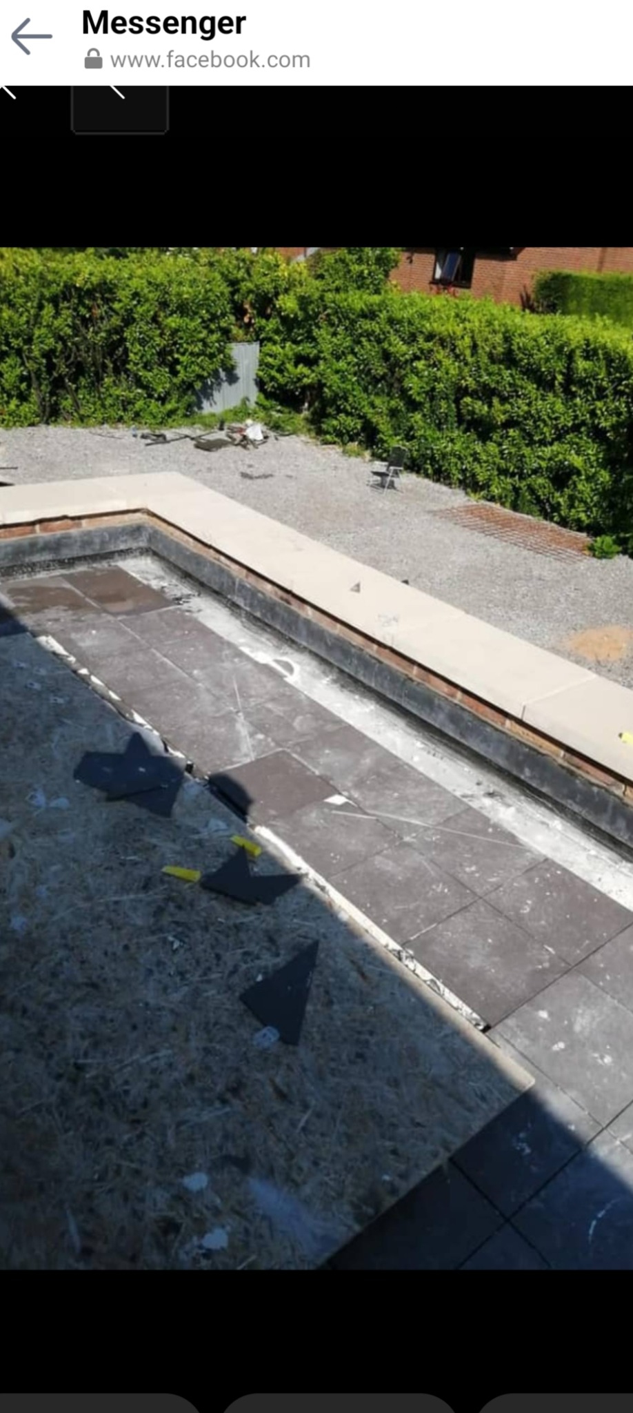 Układanie szarych płytek na podłodze tarasu, widoczne fragmenty przyciętych płytek i żółte podkładki dystansowe, w tle zielony żywopłot.