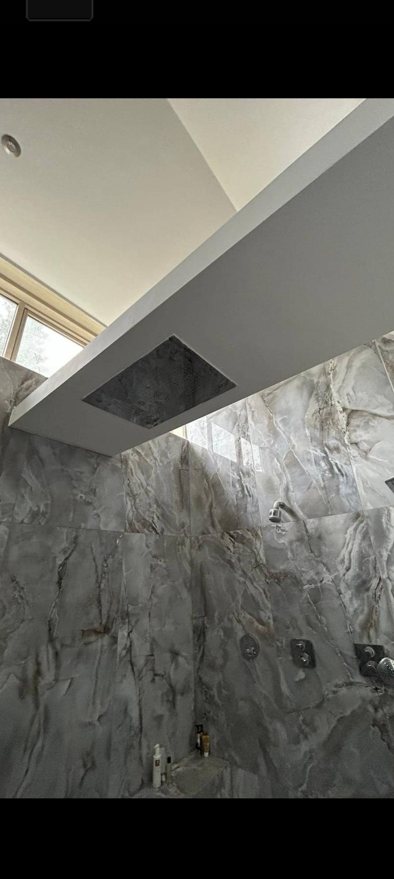Nowoczesna łazienka z deszczownicą w suficie i ścianami wyłożonymi płytkami imitującymi marmur w odcieniach szarości, widok z dołu.