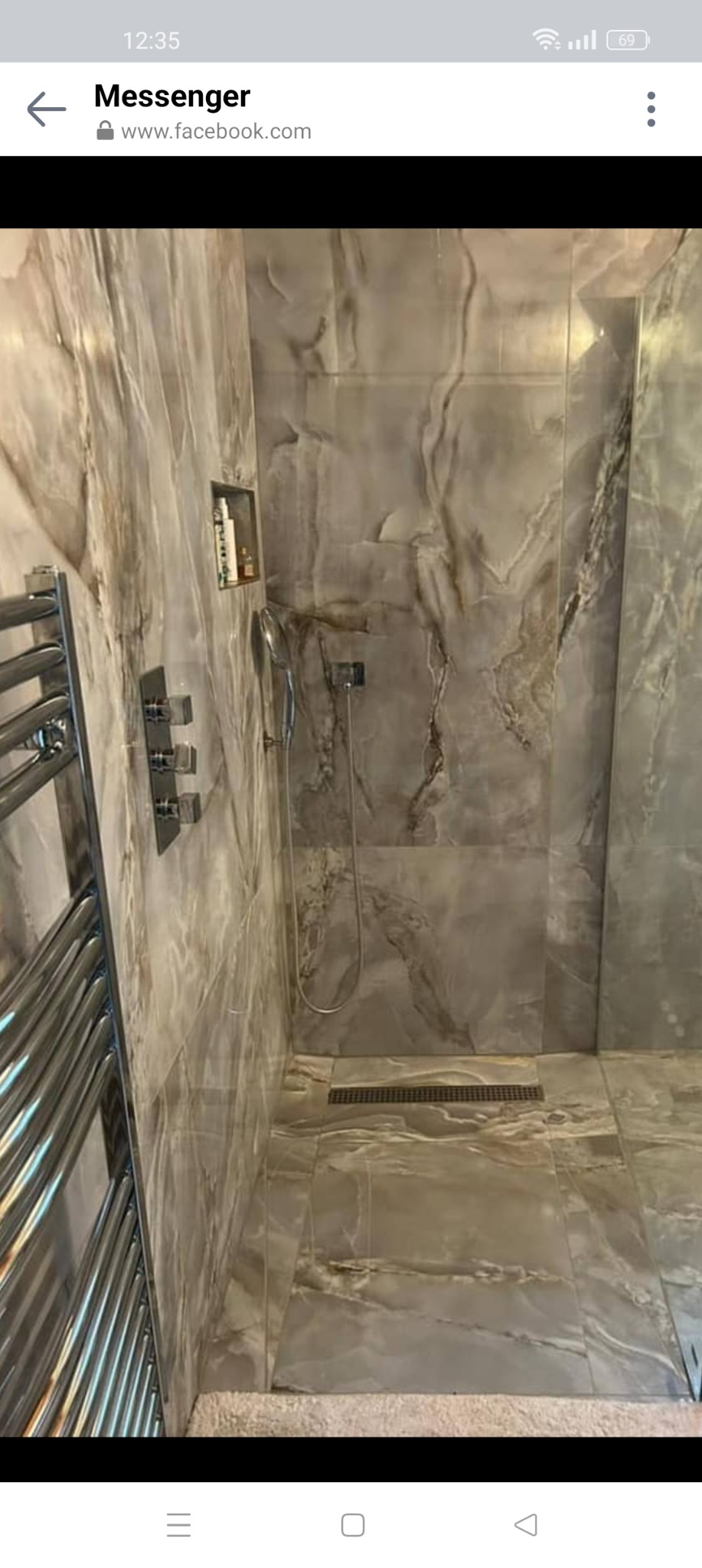 Nowoczesna kabina prysznicowa z odpływem liniowym, wykończona płytkami imitującymi marmur, z chromowaną armaturą i grzejnikiem drabinkowym.