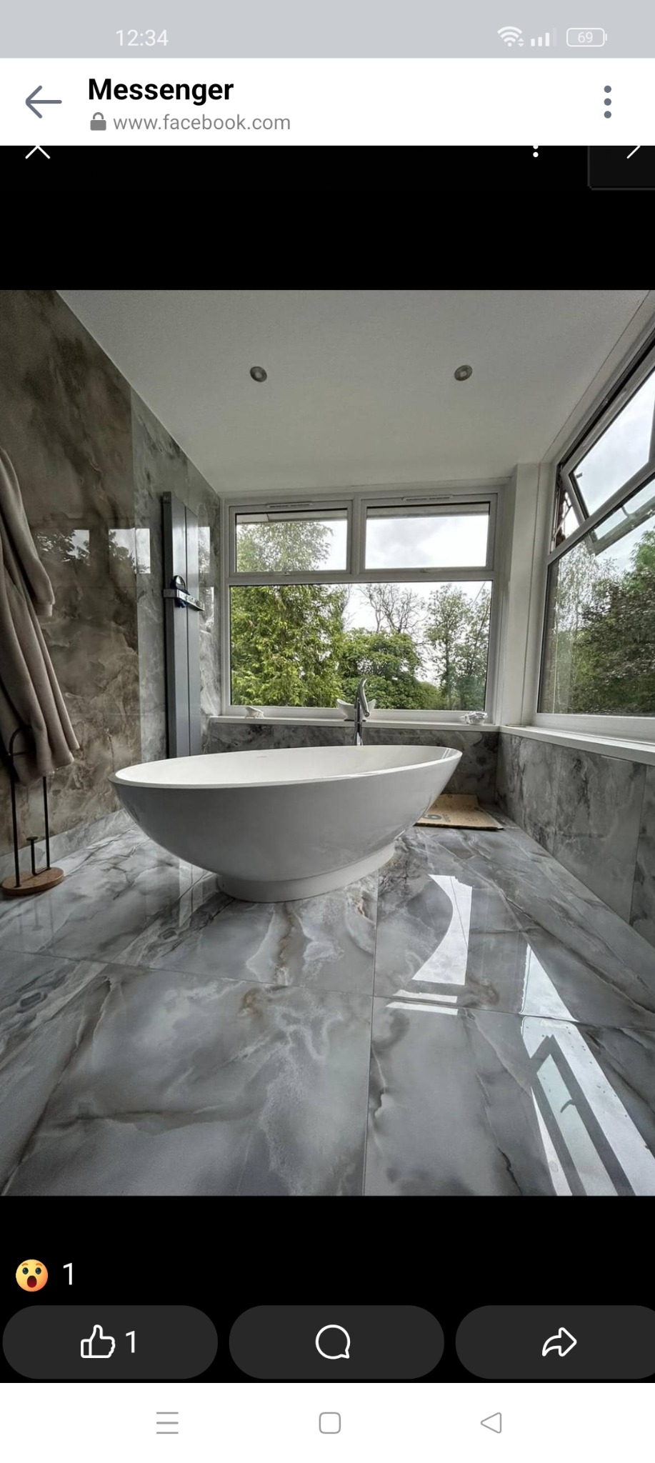 Nowoczesna łazienka z wolnostojącą wanną na tle dużego okna z widokiem na zieleń, szare płytki imitujące marmur na podłodze i ścianach, minimalistyczny grzejnik drabinkowy.