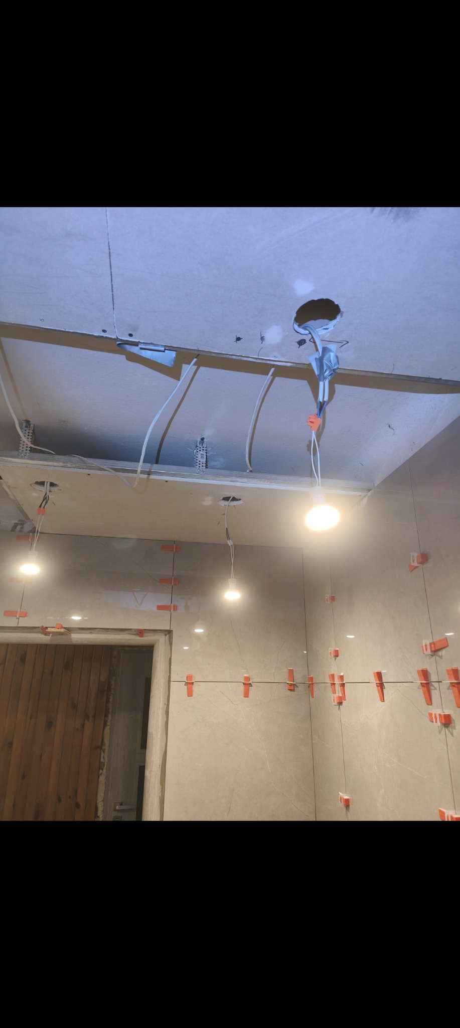 Układanie płytek w trakcie prac wykończeniowych w łazience w Łańcucie, widoczne krzyżyki dystansowe i podwieszany sufit z instalacją elektryczną.