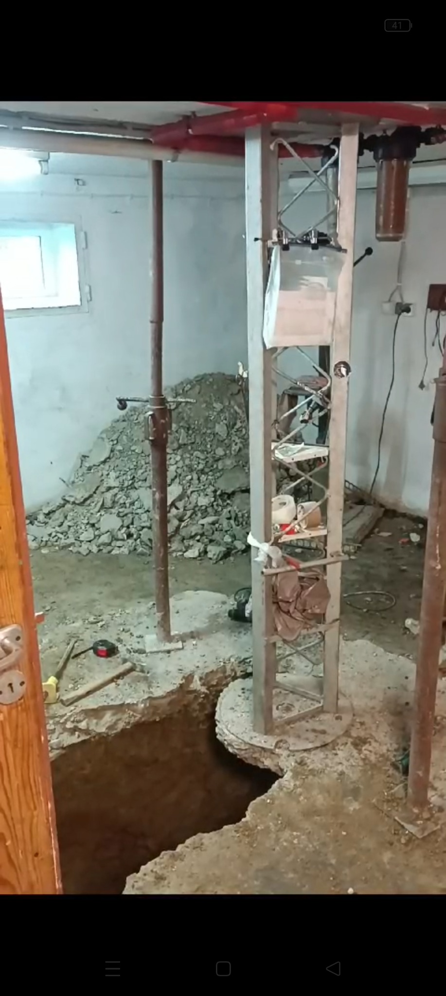 Wykop w piwnicy zabezpieczony metalową konstrukcją, widoczne narzędzia i gruz, przygotowanie do prac budowlanych.
