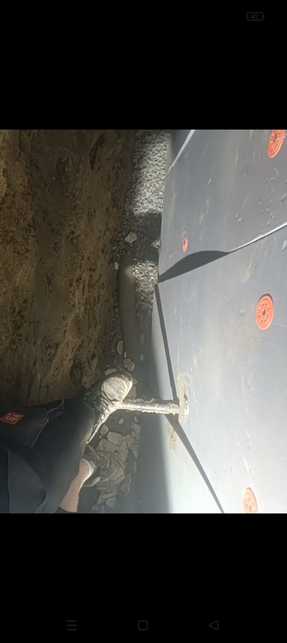 Instalacja rury w wykopie przy ścianie w Łańcucie, widoczne elementy mocujące i kamieniste podłoże.