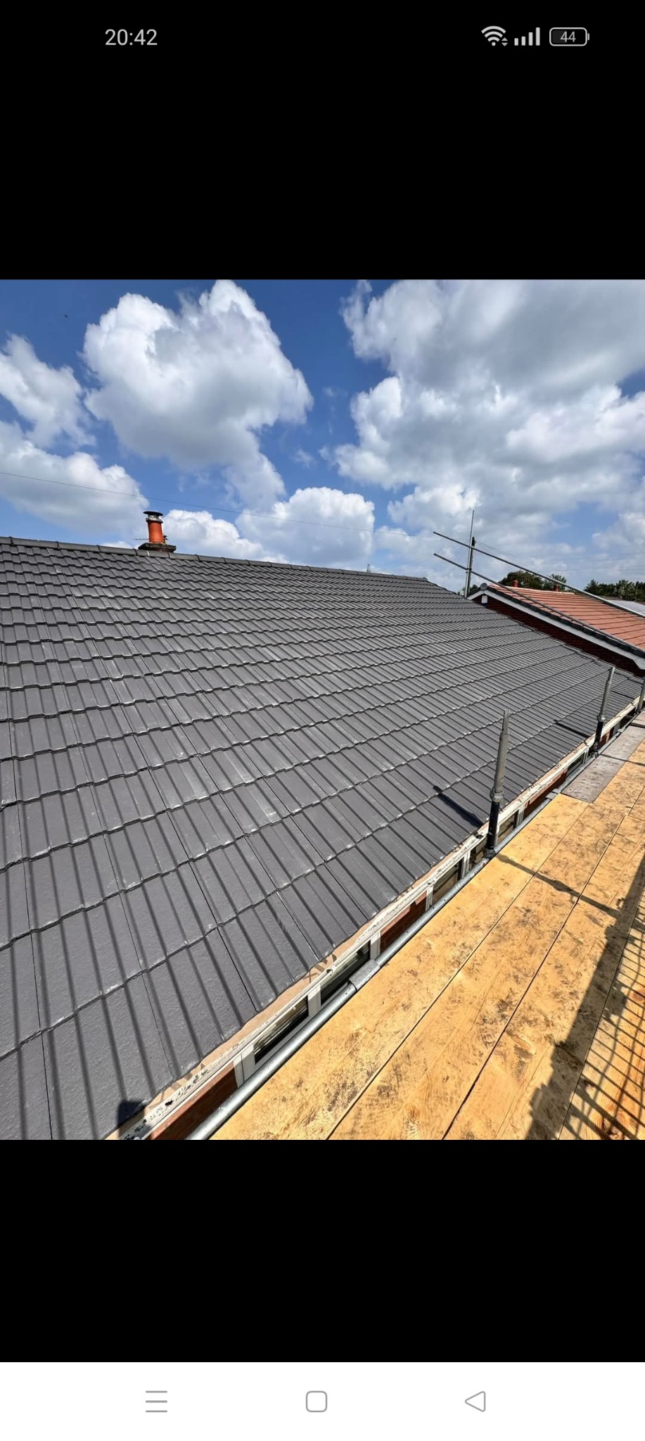 Nowy, szary dach z dachówki ceramicznej z widocznymi rusztowaniami i fragmentem nieba z chmurami.