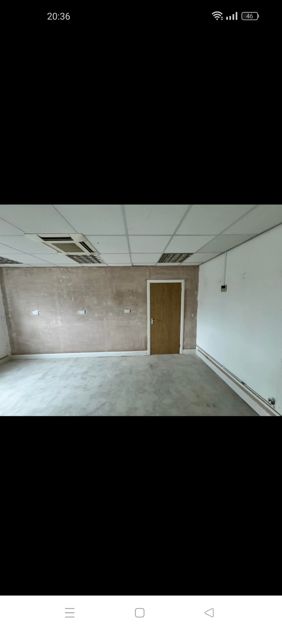 Pokój biurowy w trakcie przygotowania do malowania, ściany częściowo pokryte gładzią, widoczne puszki elektryczne, sufit podwieszany z oświetleniem rastrowym i klimatyzacją, betonowa podłoga.