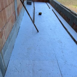 AT-BUD - Balkon w trakcie ocieplania, widoczne płyty styropianowe i poziomica laserowa, ściany z cegły ceramicznej.