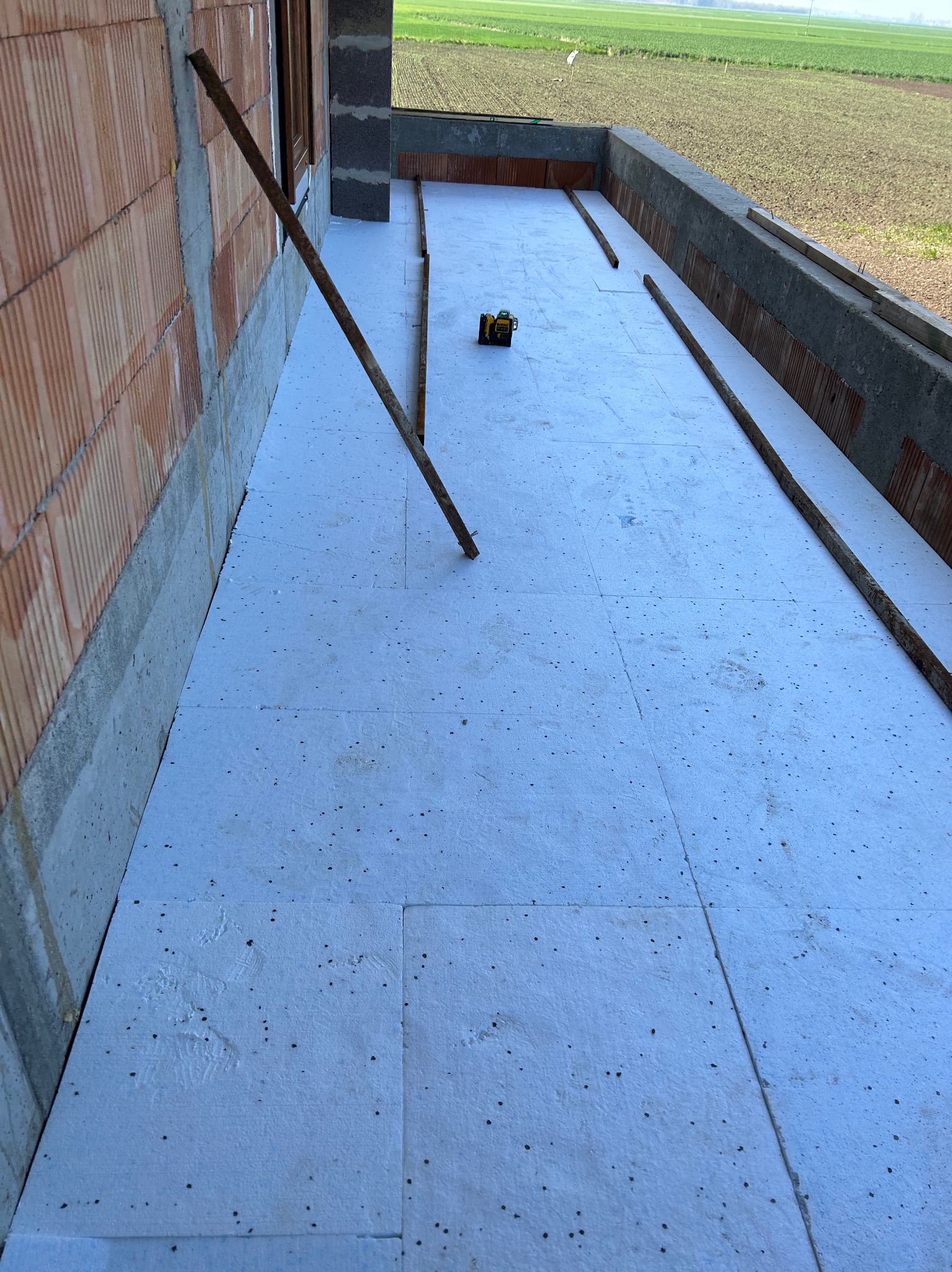 Balkon w trakcie ocieplania, widoczne płyty styropianowe i poziomica laserowa, ściany z cegły ceramicznej.