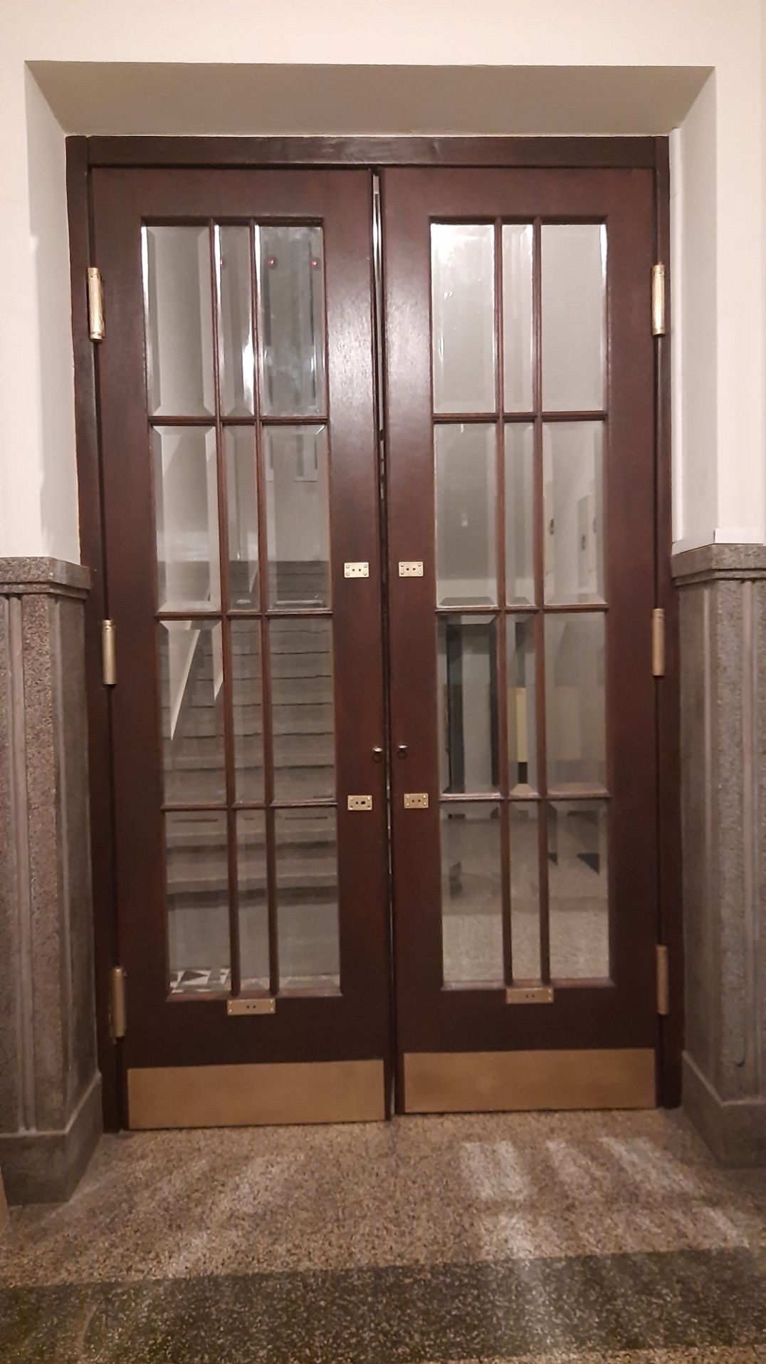 Klasyczne, dwuskrzydłowe drzwi drewniane z przeszkleniami, widoczne z bliska w Morawicy. Za drzwiami widoczne schody.