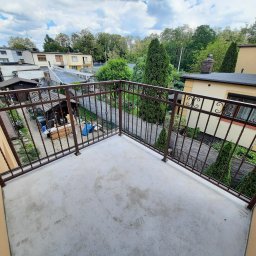 AM Metallzaune - Balkon z brązową, metalową balustradą z widokiem na podwórze z zielenią i zabudowaniami w tle, uchwycony z góry.