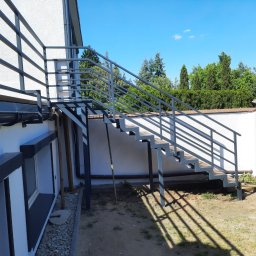 AM Metallzaune - Zewnętrzne schody z metalową konstrukcją i drewnianymi stopniami, prowadzące na balkon w Gorzowie Wielkopolskim, w słoneczny dzień.