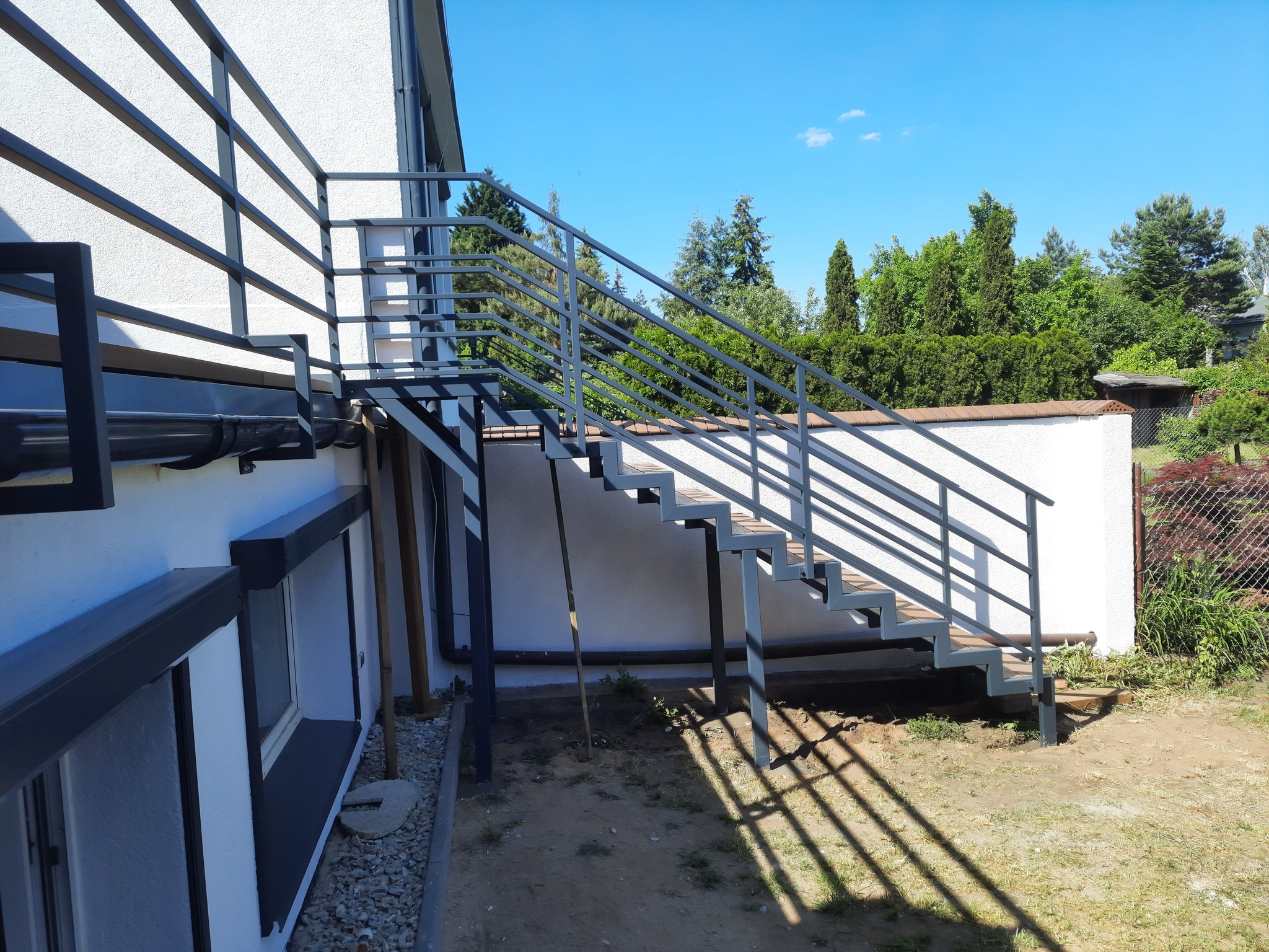 Zewnętrzne schody z metalową konstrukcją i drewnianymi stopniami, prowadzące na balkon w Gorzowie Wielkopolskim, w słoneczny dzień.