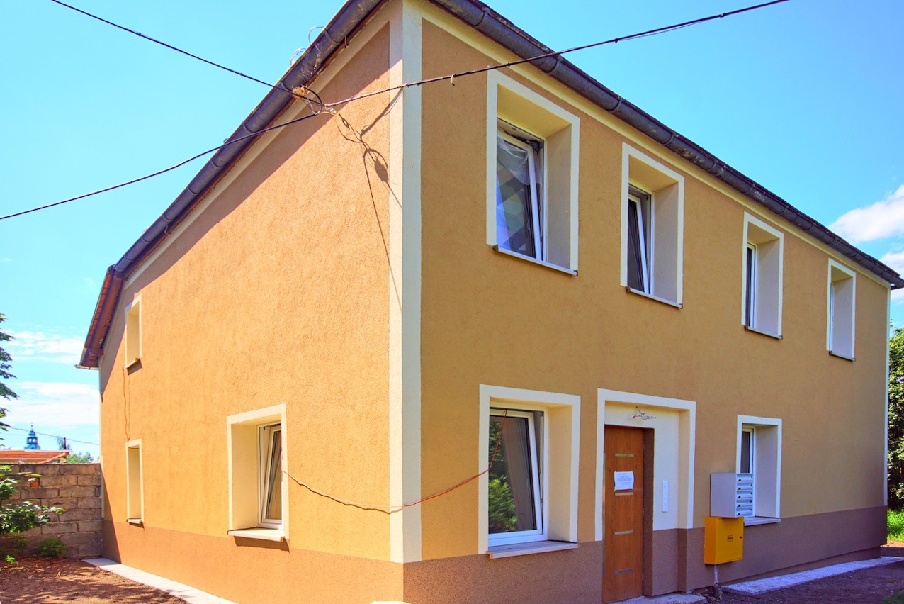 Dwupiętrowy dom z ocieploną elewacją w odcieniach beżu i brązu, z białymi obramowaniami okien i drzwi, widok z zewnątrz w słoneczny dzień.