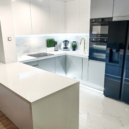 WOJCIECH GRĘBOWICZ - Nowoczesna kuchnia z białymi, błyszczącymi szafkami, szarymi dolnymi szafkami, marmurowym blatem, złotą baterią i czarną lodówką side-by-side.