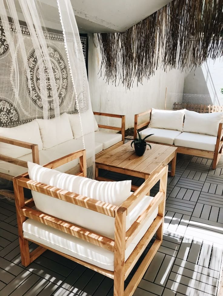 Zadaszony taras z drewnianymi meblami wypoczynkowymi z białymi poduszkami, dekoracją z suszonych traw oraz ażurową zasłoną z motywem mandali.