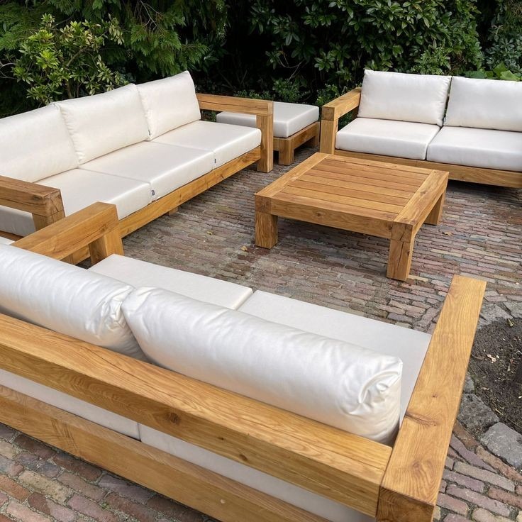 Komplet wypoczynkowy z jasnego drewna z białymi poduchami na ceglanym tarasie, widok z perspektywy dolnej.