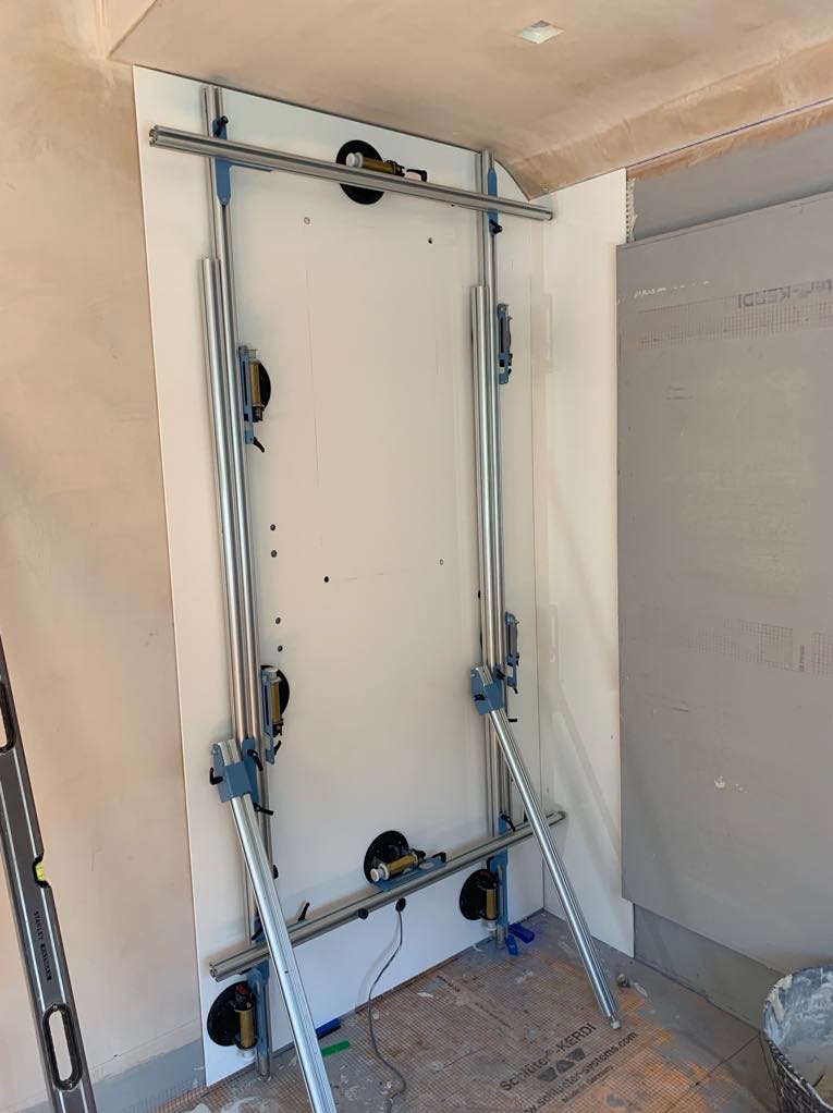 System do układania płytek wielkoformatowych na ścianie w trakcie montażu, widoczne przyssawki, aluminiowe prowadnice i płytka dociskana do ściany w surowym stanie.