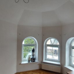 Piotr Wuttke I Andrzej Lotka - Pomalowane na biało wnętrze z trzema łukowatymi oknami, na parapecie jednego z nich ustawione wiaderka z farbą, parkiet na podłodze.