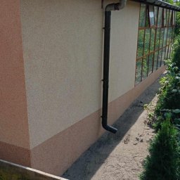 Piotr Wuttke I Andrzej Lotka - Elewacja budynku z oknami szklarniowymi, dwukolorowym tynkiem i czarną rynną spustową, widok z zewnątrz.