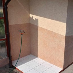 Piotr Wuttke I Andrzej Lotka - Zewnętrzny prysznic z wyłożoną płytkami podłogą, dwukolorową elewacją i zielonym wężem ogrodowym.