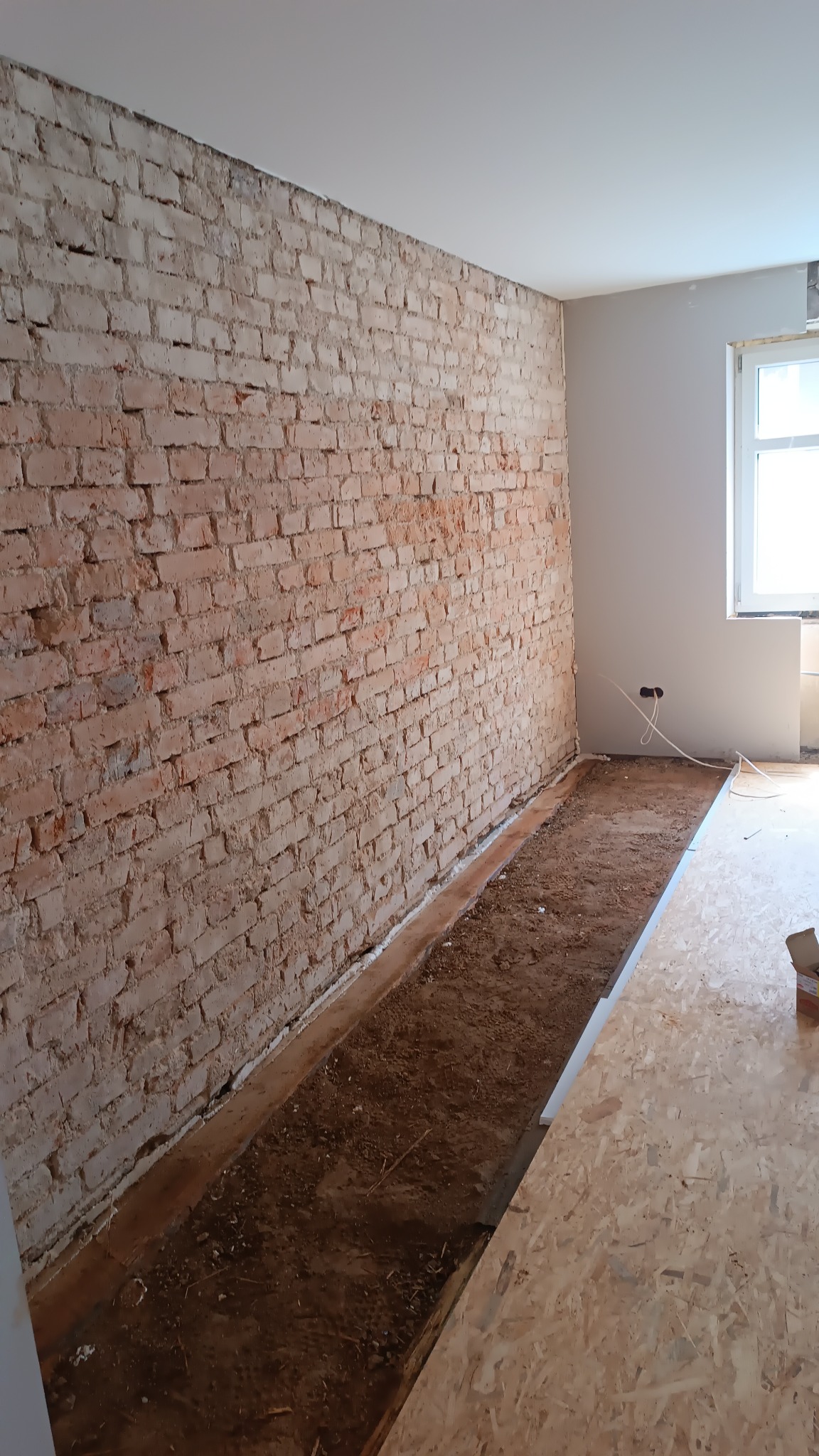 Ceglana ściana w trakcie remontu w Chojnowie, widoczne przygotowane podłoże pod wylewkę i płyty OSB, gniazdka elektryczne wystają ze ściany.