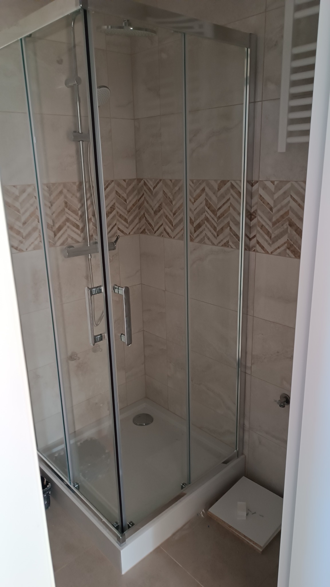 Kabina prysznicowa z chromowanymi okuciami i deszczownicą na tle beżowych płytek z dekoracyjnym pasem w jodełkę, widoczna po zakończeniu prac.