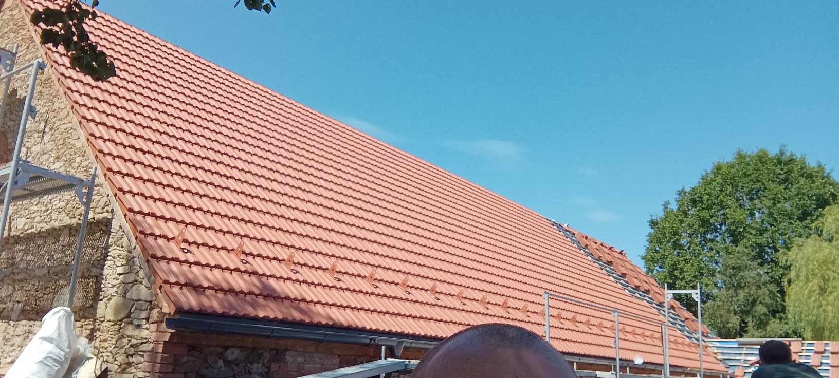 Nowy, czerwony dach z dachówki ceramicznej na budynku w Jeleniej Górze, widok z dołu z fragmentem rusztowania i niebieskim niebem w tle.