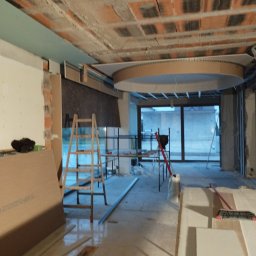 Usługi remontowe Patryk Nowacki - Wnętrze w trakcie prac wykończeniowych: widoczny surowy strop z cegły, okrągła konstrukcja podwieszana, płyty gipsowo-kartonowe, drabina i narzędzia na podłodze.