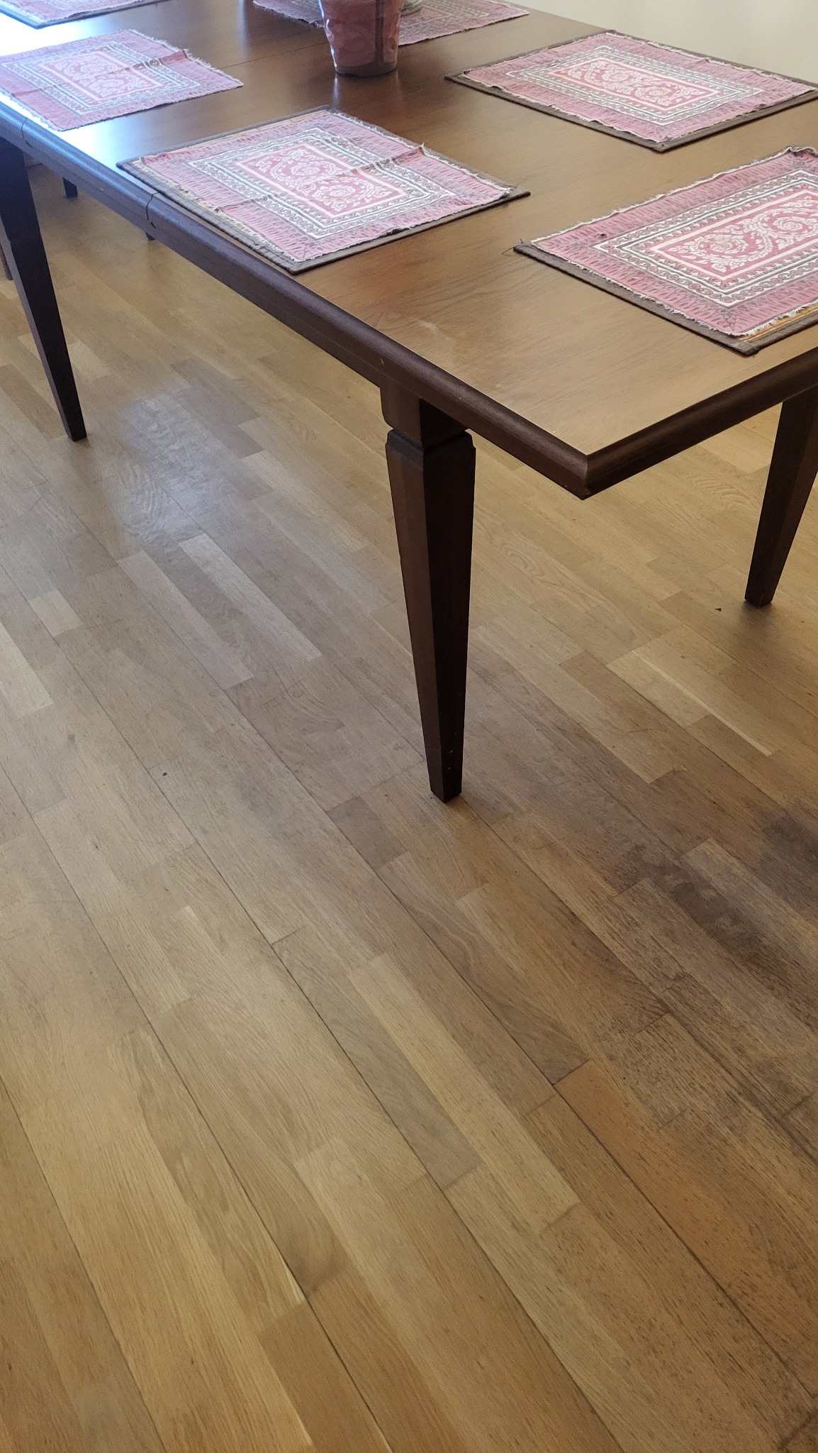 Wypolerowany drewniany stół z czterema podkładkami w odcieniach różu i beżu, ustawiony na parkiecie z jasnego drewna. Widok z góry, oświetlenie naturalne.