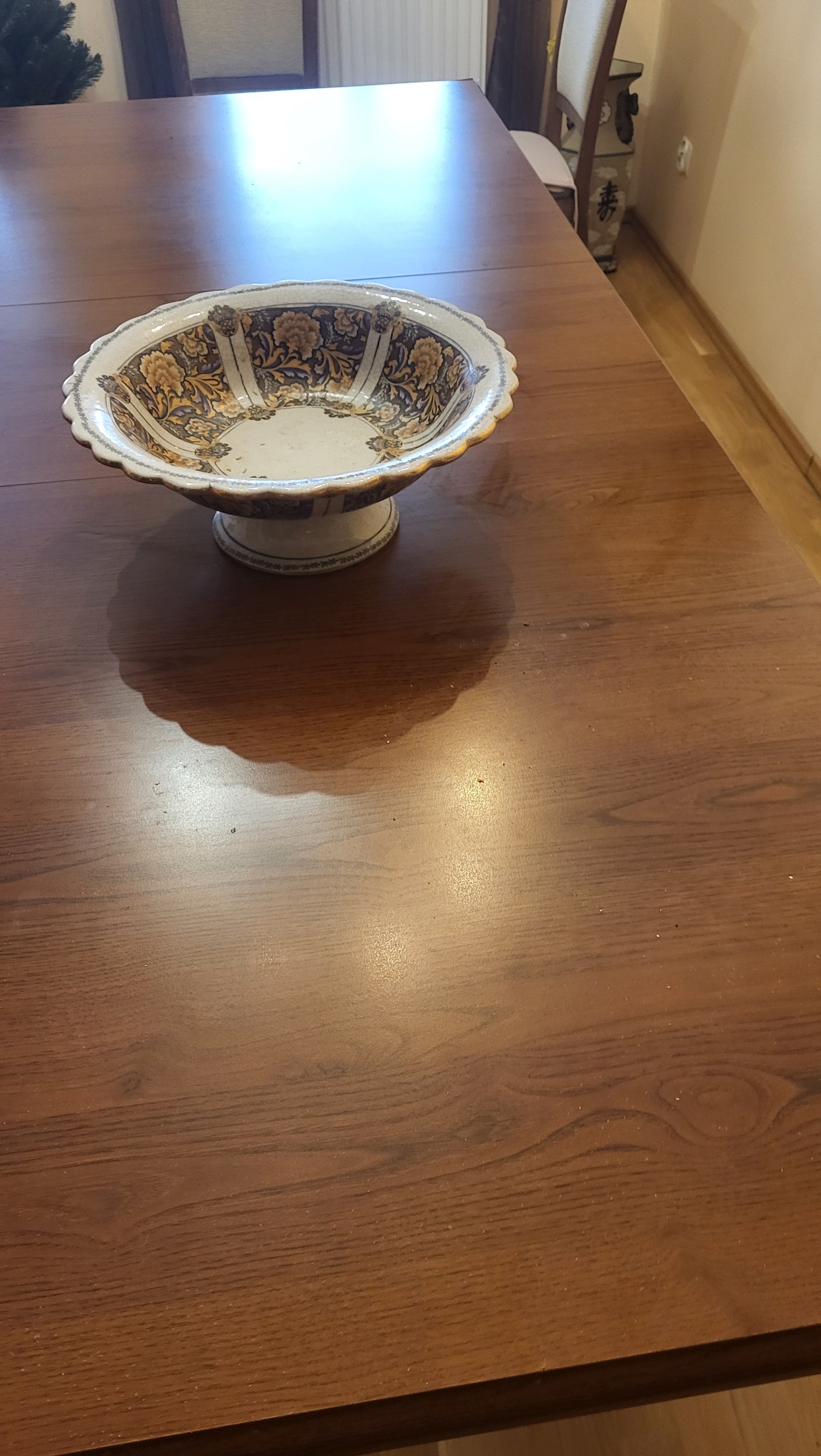 Patera dekoracyjna z motywem kwiatowym na drewnianym stole. Widoczne drobne zabrudzenia wewnątrz naczynia. Ujęcie z góry, oświetlenie naturalne.