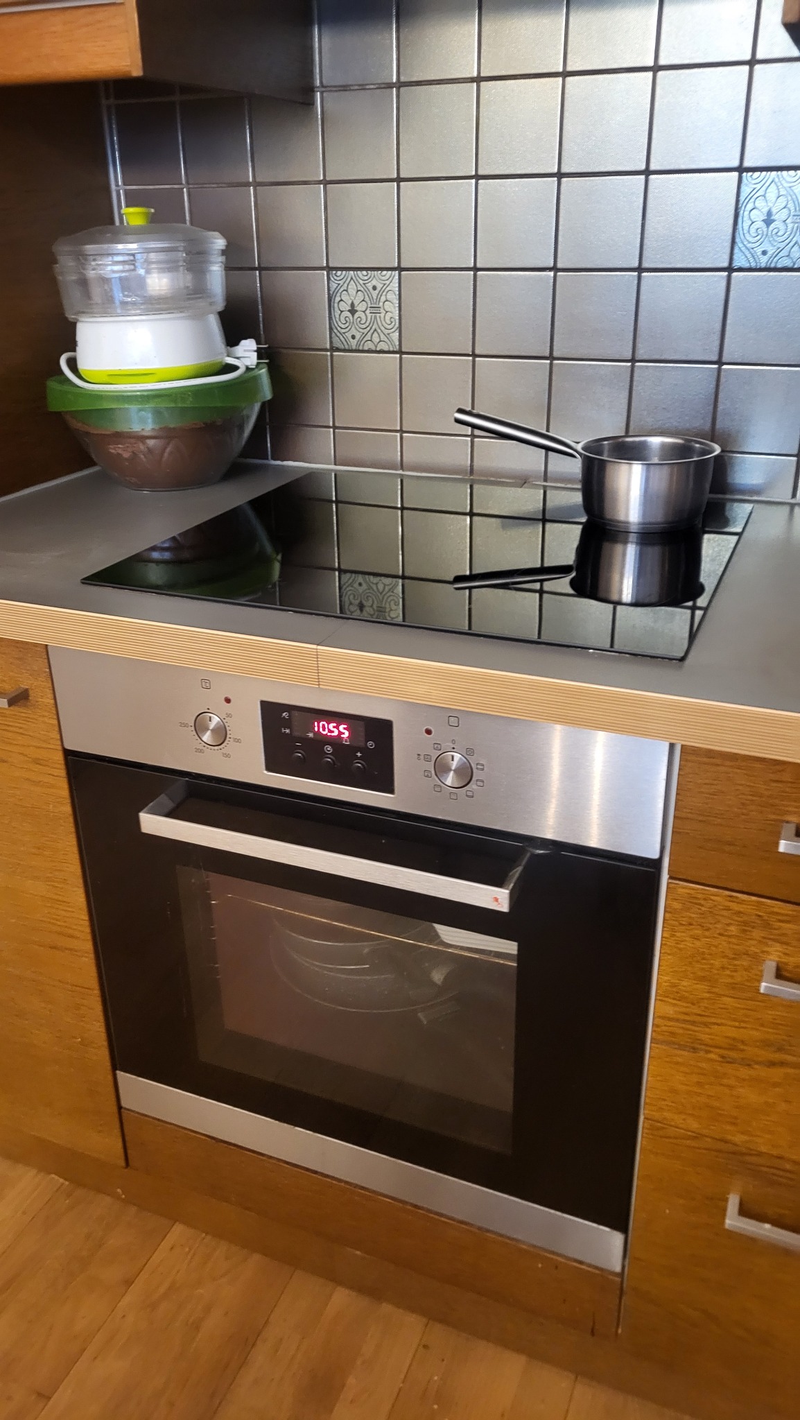 Umyta płyta indukcyjna z garnkiem, czysty blat i piekarnik w kuchni z szarymi płytkami. Widok po sprzątaniu, z bliska.