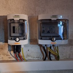 ELEKTRO-CIERBIKOWSKI KRYSTIAN CIERBIKOWSKI - Dwa białe rozdzielacze elektryczne marki Noark, model KENO, zamontowane na szarej, nierównej ścianie z widocznymi przewodami w kolorach czarnym, czerwonym i żółto-zielonym, umieszczone na białej...