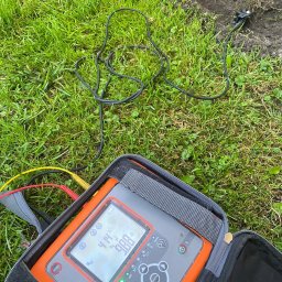 ELEKTRO-CIERBIKOWSKI KRYSTIAN CIERBIKOWSKI - Miernik rezystancji uziomu Sonel MRU-30 w otwartym futerale na trawie, z widocznymi przewodami pomiarowymi i sondą wbita w ziemię, podczas pomiaru rezystancji.