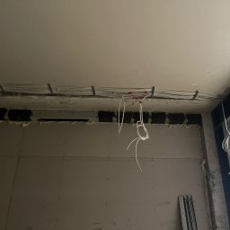 ELEKTRO-CIERBIKOWSKI KRYSTIAN CIERBIKOWSKI - Wiązka przewodów elektrycznych prowadzona pod sufitem w trakcie prac wykończeniowych w Chełmie Śląskim, widoczne uchwyty mocujące i wystające końcówki kabli.