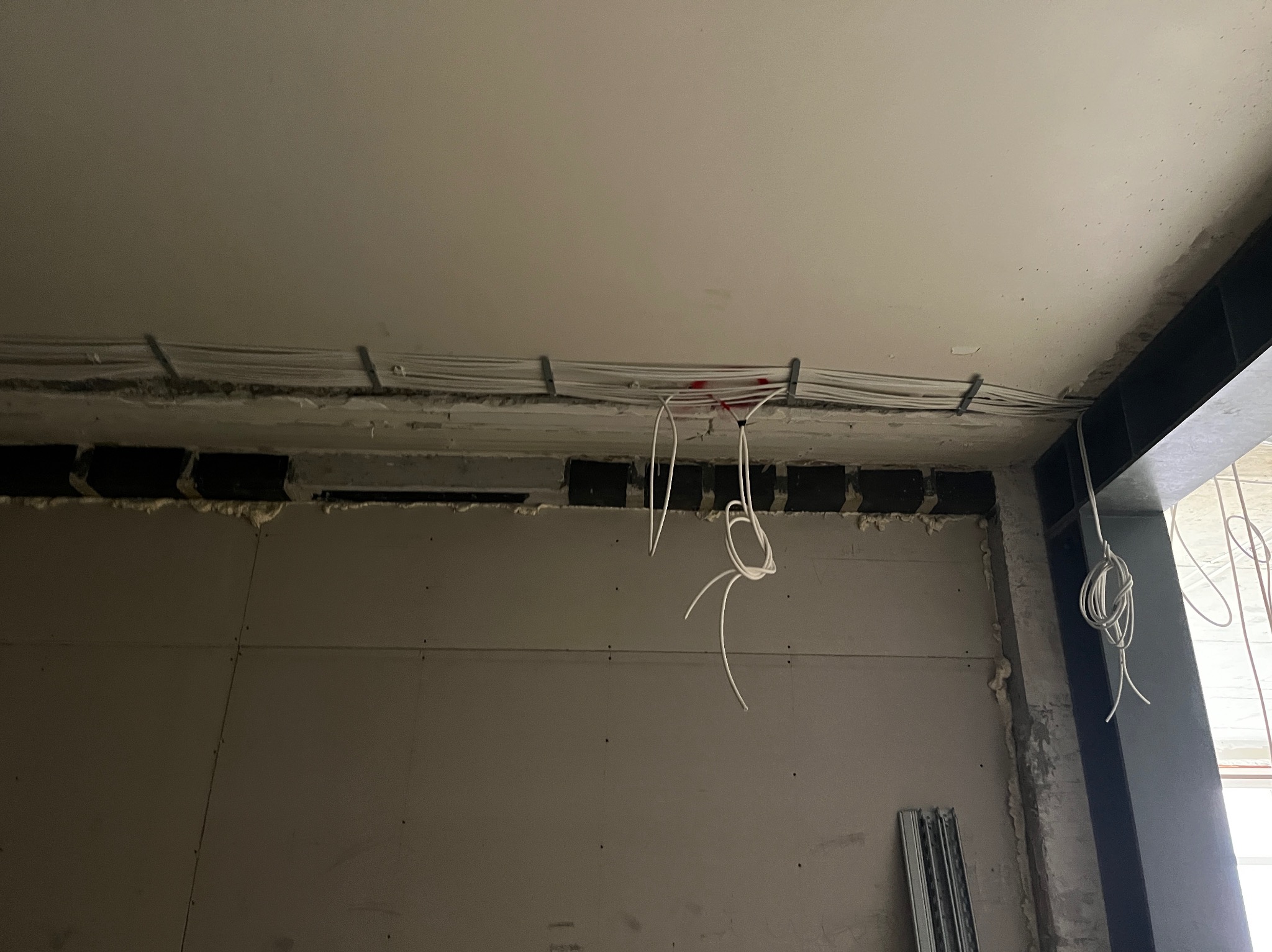 Wiązka przewodów elektrycznych prowadzona pod sufitem w trakcie prac wykończeniowych w Chełmie Śląskim, widoczne uchwyty mocujące i wystające końcówki kabli.